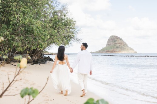 Matias Ezcurra Photography, Klaire and Alex hold hands, walking on a Kualoa Ranch beach toward the ocean.