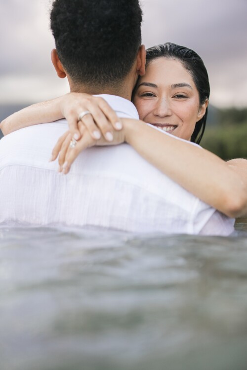 Matias Ezcurra Photography, Happy couple embracing in water at their Kualoa Ranch wedding.
