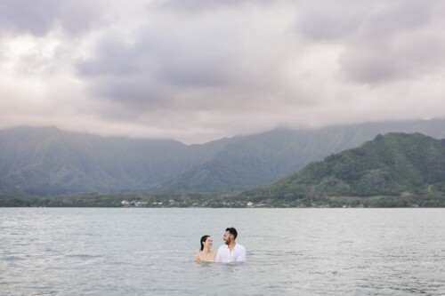 Matias Ezcurra Photography, Happy couple in white clothing wading in calm ocean water at Kualoa Ranch, Hawaii.