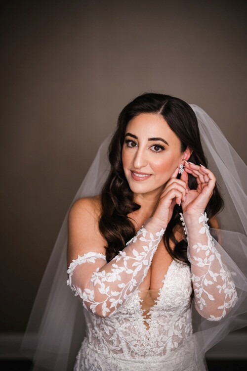 Matias Ezcurra Photography, Bride in lace wedding dress puts on earrings