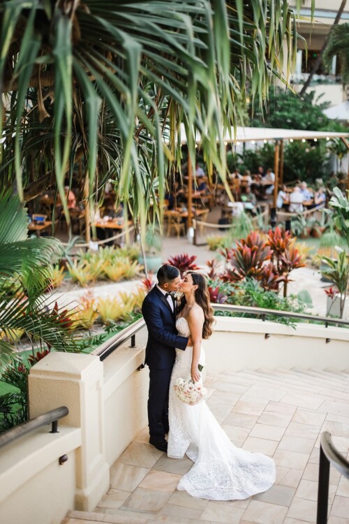 Matias Ezcurra Photography, Bride and groom kissing on a patio, tropical plants in background.