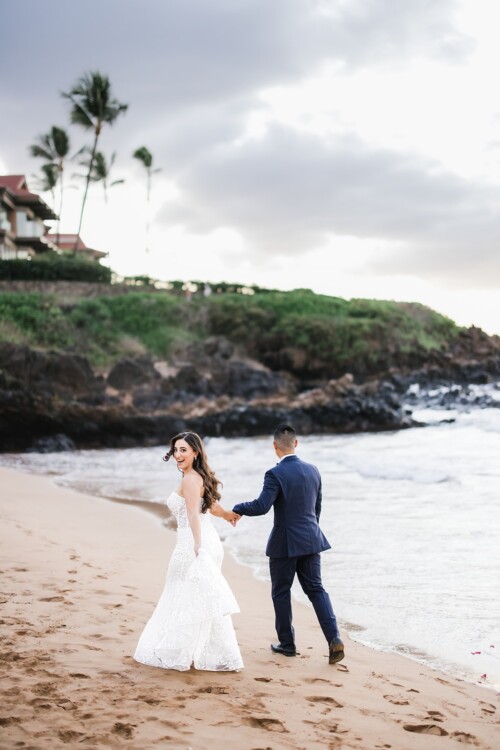 Matias Ezcurra Photography, Bride and groom holding hands, walking away on a beach at sunset.