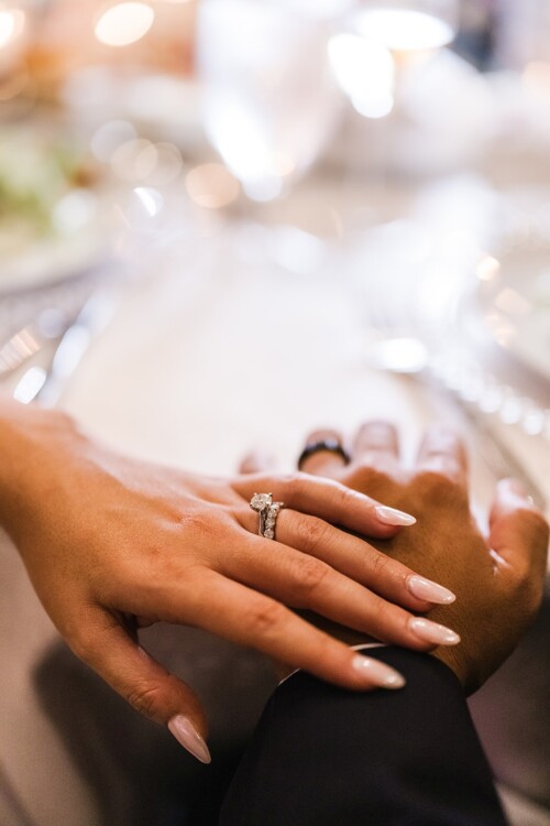 Matias Ezcurra Photography, Close-up of a bride and groom's hands clasped together, showcasing her diamond engagement and wedding rings.