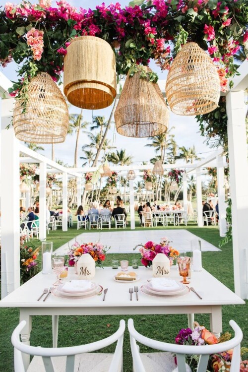 Matias Ezcurra Photography, Romantic sweetheart table at an Andaz Maui wedding, decorated with woven lanterns and vibrant floral arrangements. "Mr." and "Mrs." place cards are visible.