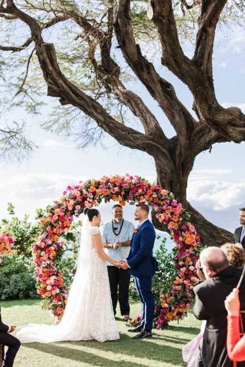 Matias Ezcurra Photography, Serra & Kevin exchange vows at their Andaz Maui wedding ceremony, beneath a vibrant floral arch.