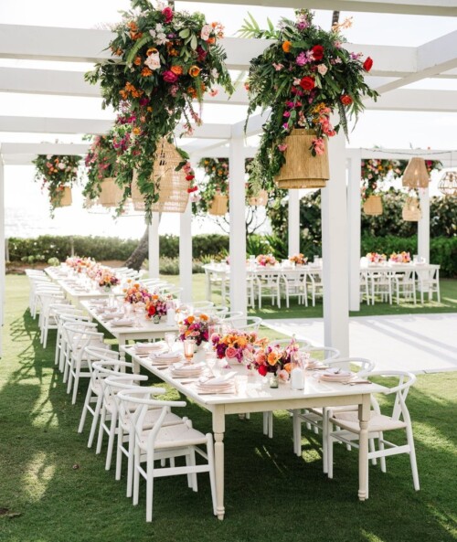 Matias Ezcurra Photography, Elegant outdoor wedding reception at Andaz Maui with long tables, white chairs, and vibrant floral arrangements hanging from a pergola.
