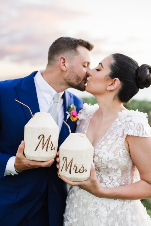 Matias Ezcurra Photography, Bride and groom at their Andaz Maui wedding, sharing a celebratory kiss and coconut drinks labeled "Mr." and "Mrs.